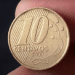 Uma moeda brasileira de 10 centavos do ano 2000, segurada entre os dedos, mostrando a data de cunhagem e o busto de Tiradentes no reverso.