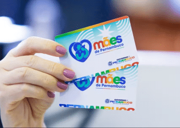 Mãos segurando cartão do programa Mães de Pernambuco mostrando logotipo colorido do benefício social