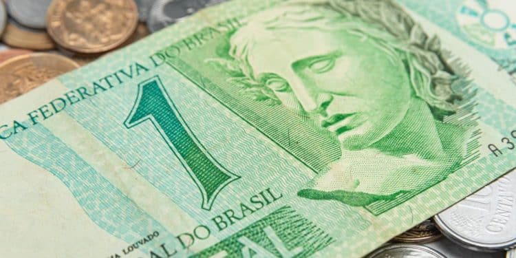 Close-up da cédula brasileira de 1 Real de cor verde, com a efígie da República, sobreposta a moedas, ilustrando uma nota procurada por colecionadores (numismatas).
