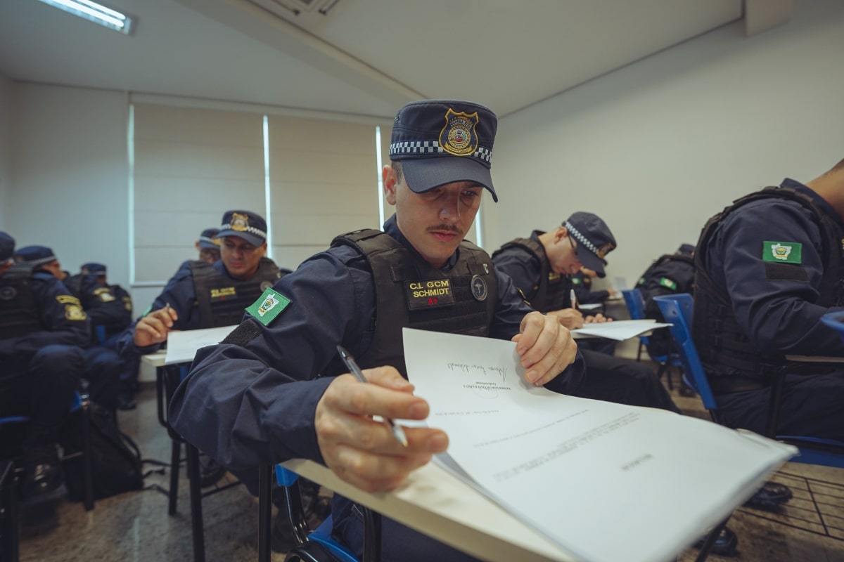 Guarda Municipal uniformizado concentrado preenchendo documentos dentro de sala de aula durante treinamento