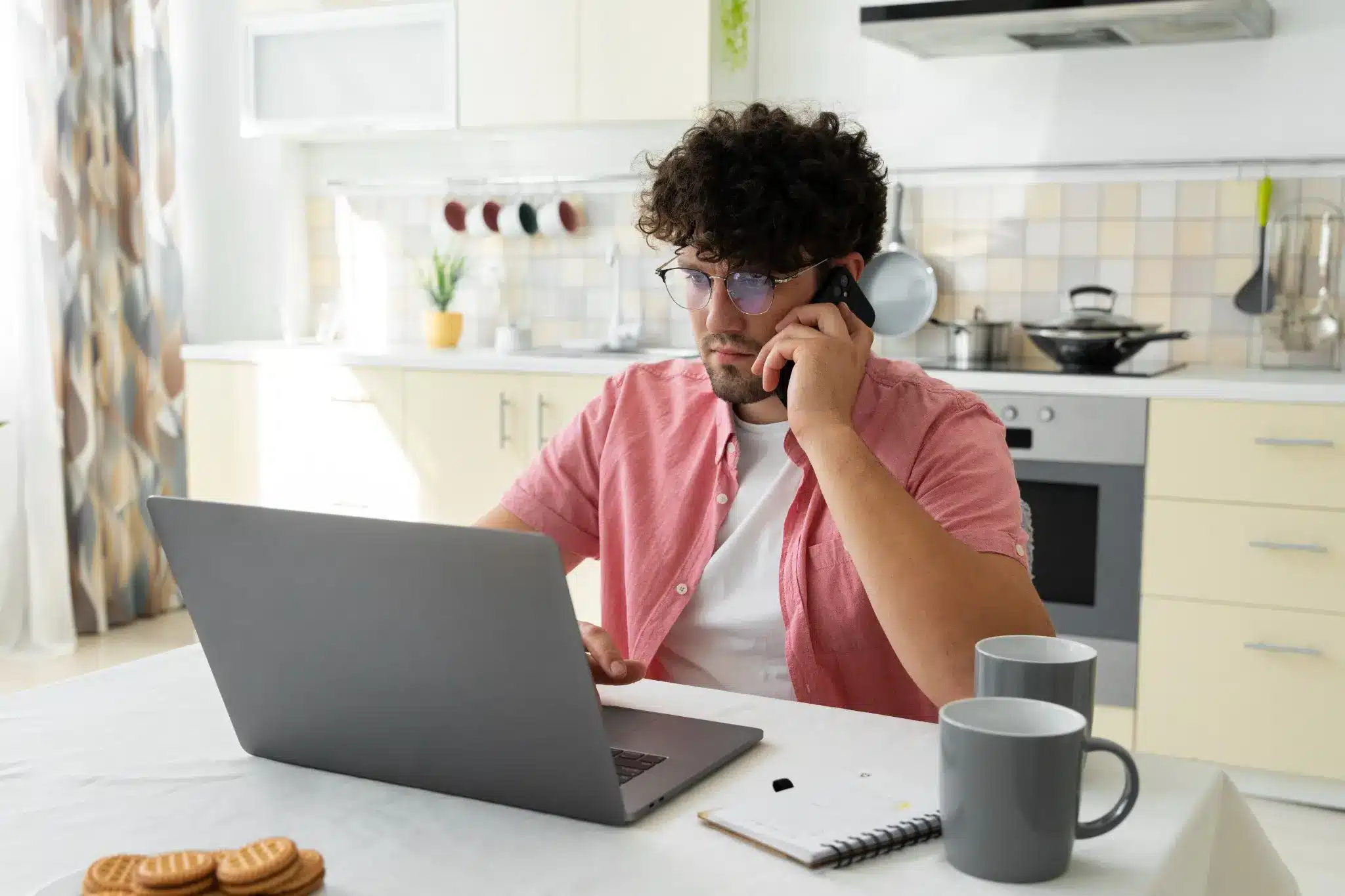Homem trabalhando de home office, falando no telefone e utilizando um laptop, representando a busca por especializações online e plataformas de trabalho remoto.