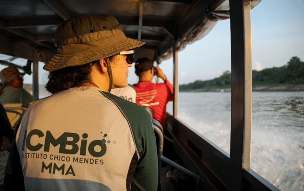 Mulher com camisa do ICMBio e chapéu de pescador em barco navegando por rio com outras pessoas.