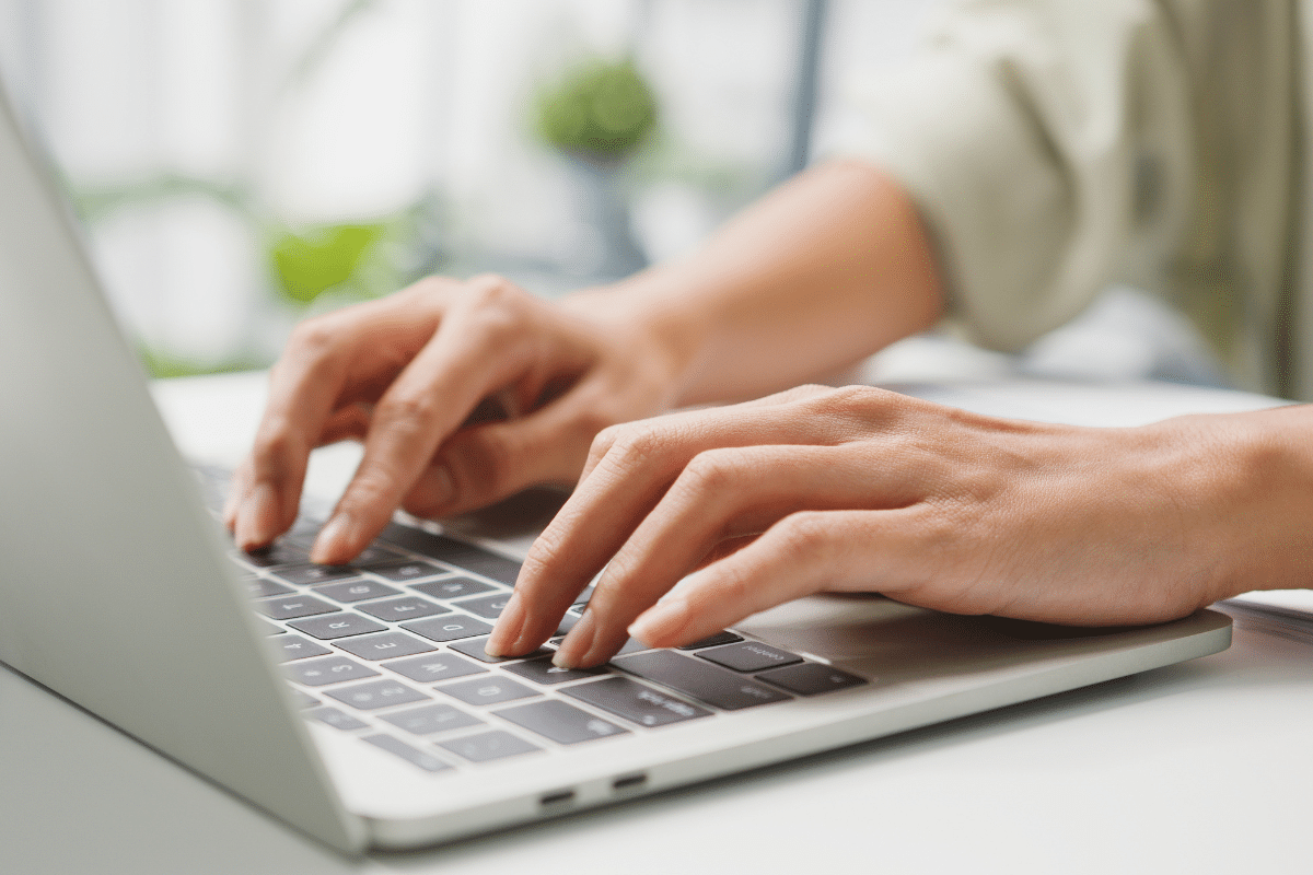 Imagem de mãos femininas digitando em teclado de laptop em ambiente claro e profissional