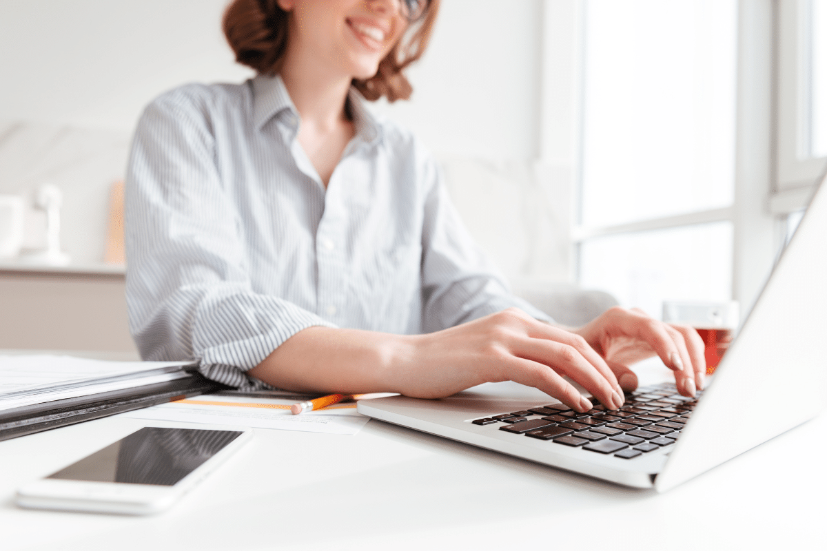  Pessoa sorridente usando camisa listrada enquanto digita em laptop em ambiente claro e organizado