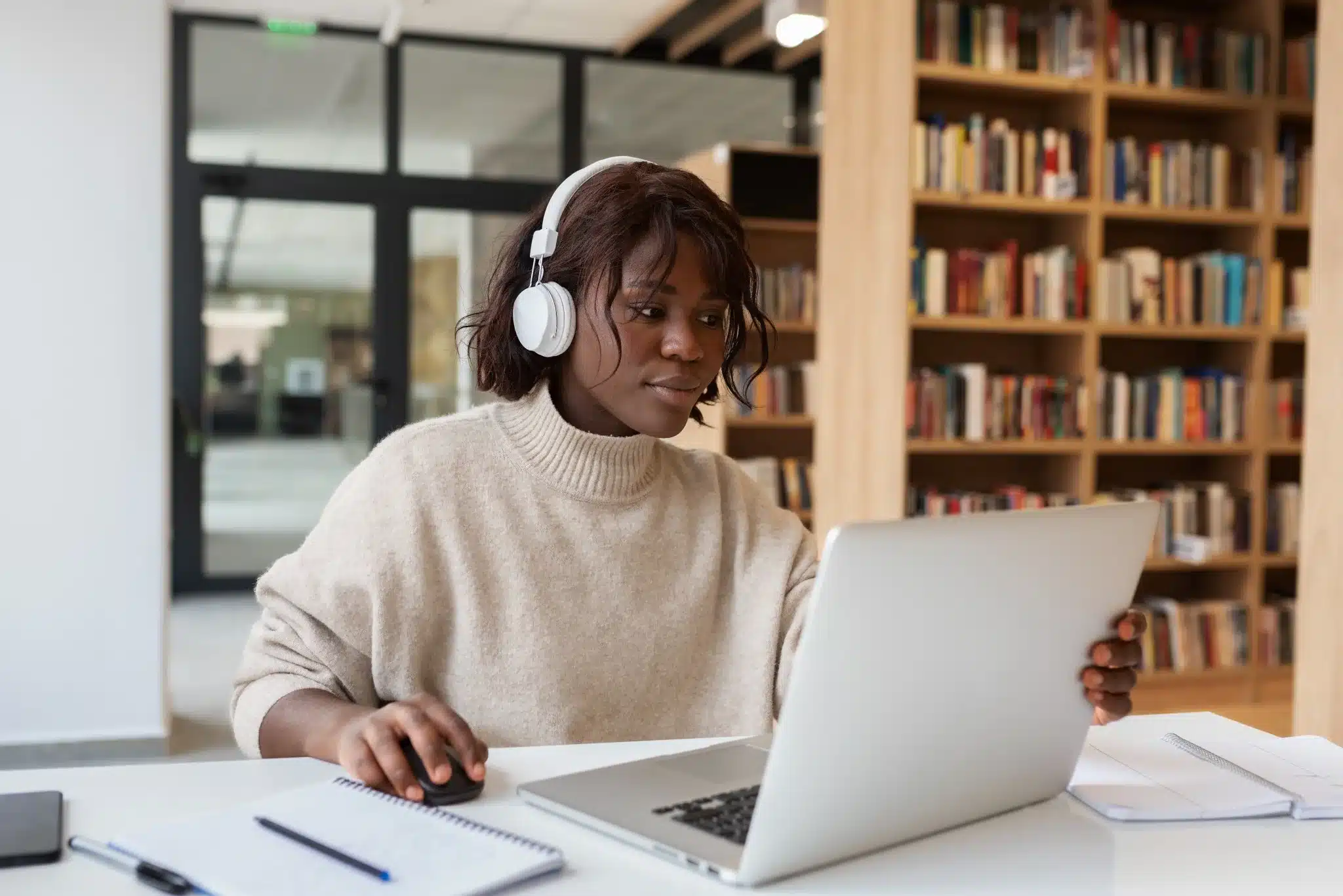 Jovem estudante utilizando computador portátil com fones de ouvido em ambiente de biblioteca, ilustrando a popularização dos cursos EAD no Brasil.