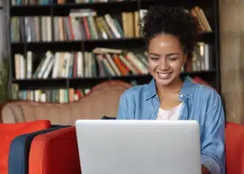 Mulher sorridente usando um laptop em um ambiente de biblioteca, representando o crescimento do número de alunos em EAD.