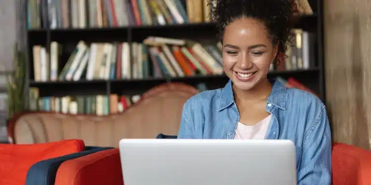 Mulher sorridente usando um laptop em um ambiente de biblioteca, representando o crescimento do número de alunos em EAD.