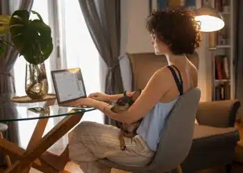 Pessoa trabalhando em casa no computador com cachorro de estimação no colo, ilustrando profissões home office.