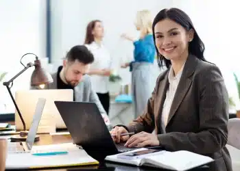 Mulher trabalhando em um escritório moderno em frente ao computador, com foco em profissões sem exigência de diploma.
