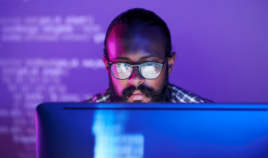 Profissional concentrado diante de monitor com códigos refletidos nos óculos