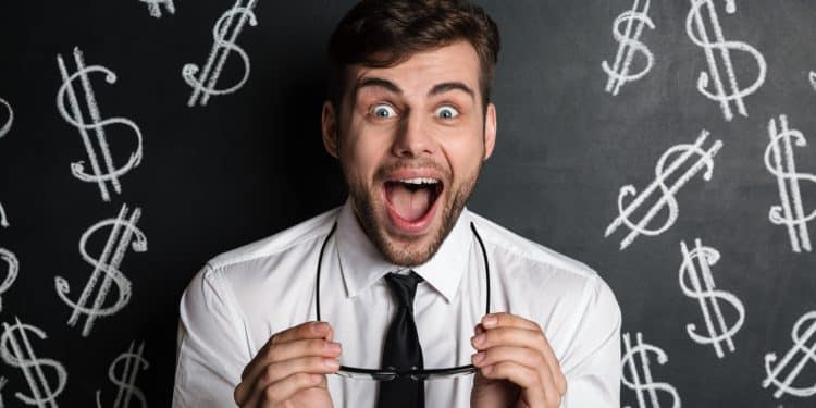 Homem de camisa branca e gravata preta surpreso segurando óculos com fundo de quadro negro e símbolos de dólar desenhados.