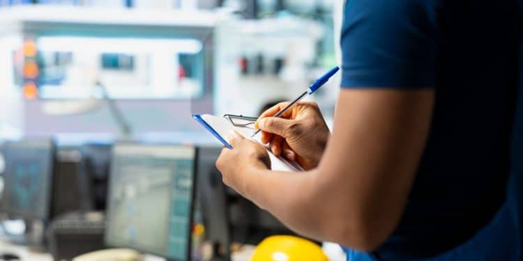 Profissional técnico fazendo anotações em ambiente industrial com equipamentos ao fundo