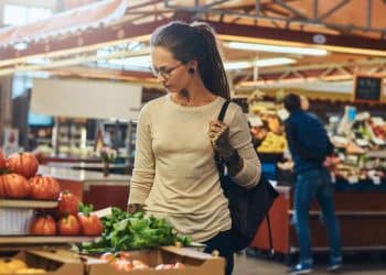 Mulher comprando verduras frescas em feira ou mercado coberto após queda de preços da cesta básica em setembro