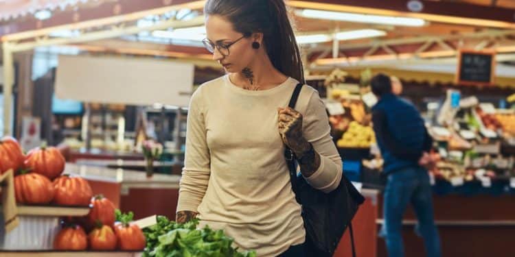 Mulher comprando verduras frescas em feira ou mercado coberto após queda de preços da cesta básica em setembro