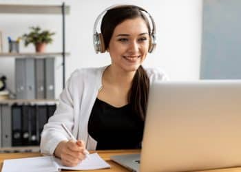 Jovem profissional participando de curso online gratuito em ambiente doméstico com computador e fones de ouvido