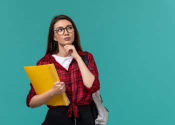 Estudante pensativa segura uma pasta amarela e reflete sobre a escolha entre curso técnico e faculdade.