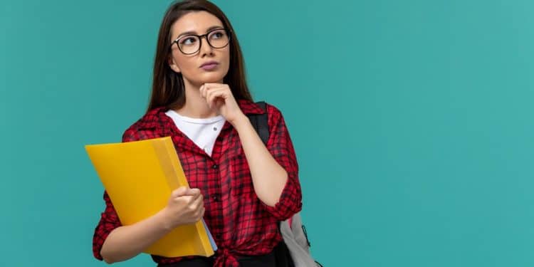 Estudante pensativa segura uma pasta amarela e reflete sobre a escolha entre curso técnico e faculdade.