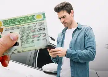 Homem segurando sua Carteira Nacional de Habilitação (CNH) física enquanto utiliza o smartphone para acessar informações sobre o documento.