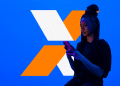 Mulher negra com tranças segurando smartphone com fundo azul e logo laranja e branco.