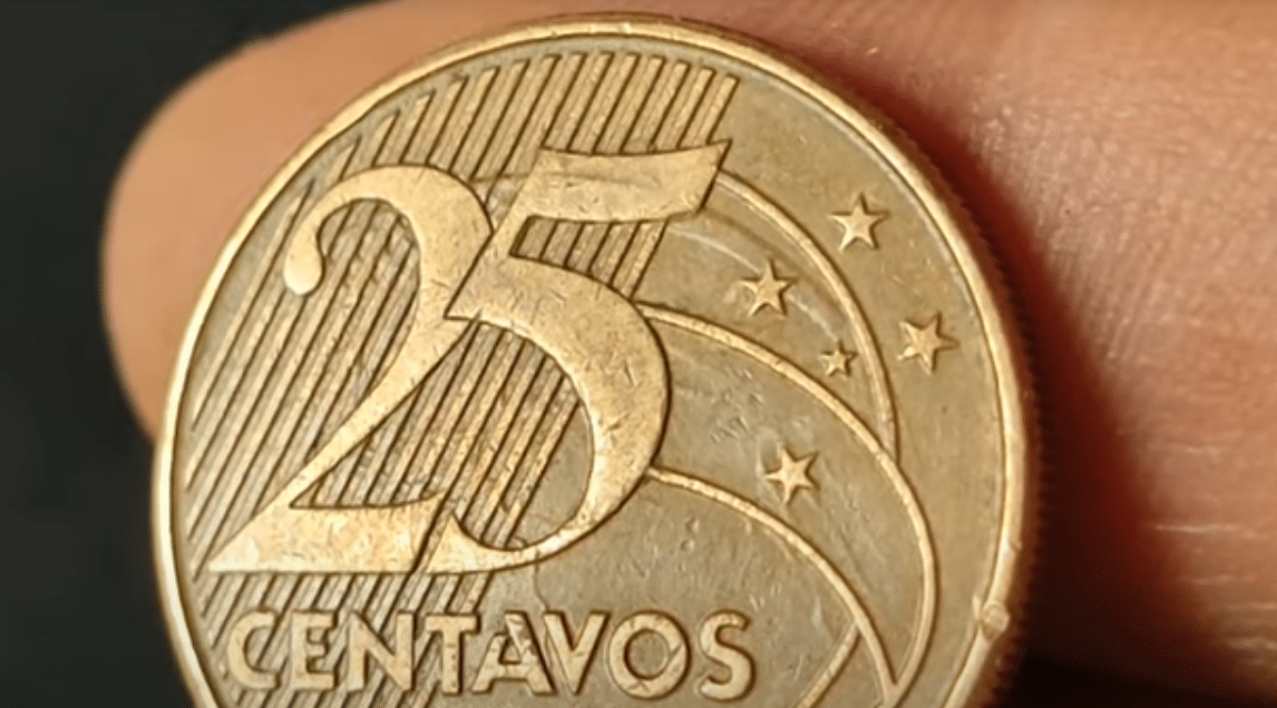 Close-up da moeda de 25 centavos, focando na região das estrelas onde o erro de "rastros" de cunhagem pode ser encontrado.