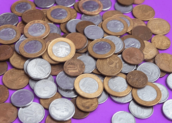 Imagem de moedas do Real espalhadas, com destaque para a moeda de 1 Real de 2018, que pode ser rara devido a erro de cunhagem.