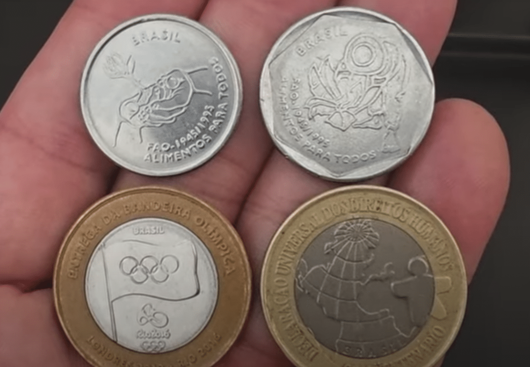 Quatro moedas raras e comemorativas do Brasil, incluindo a Moeda da Bandeira Olímpica e a DH, exemplificando o potencial de valorização do Real.