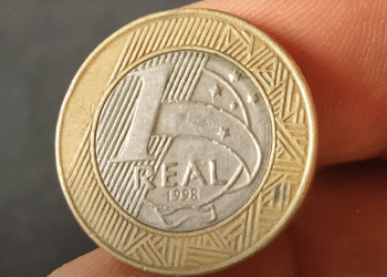 Close-up da moeda de 1 Real do ano 1998, destacando o anverso e a data. A peça é procurada por colecionadores devido a possíveis erros de cunhagem, como o reverso inclinado.