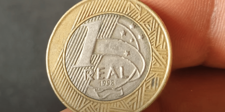 Close-up da moeda de 1 Real do ano 1998, destacando o anverso e a data. A peça é procurada por colecionadores devido a possíveis erros de cunhagem, como o reverso inclinado.