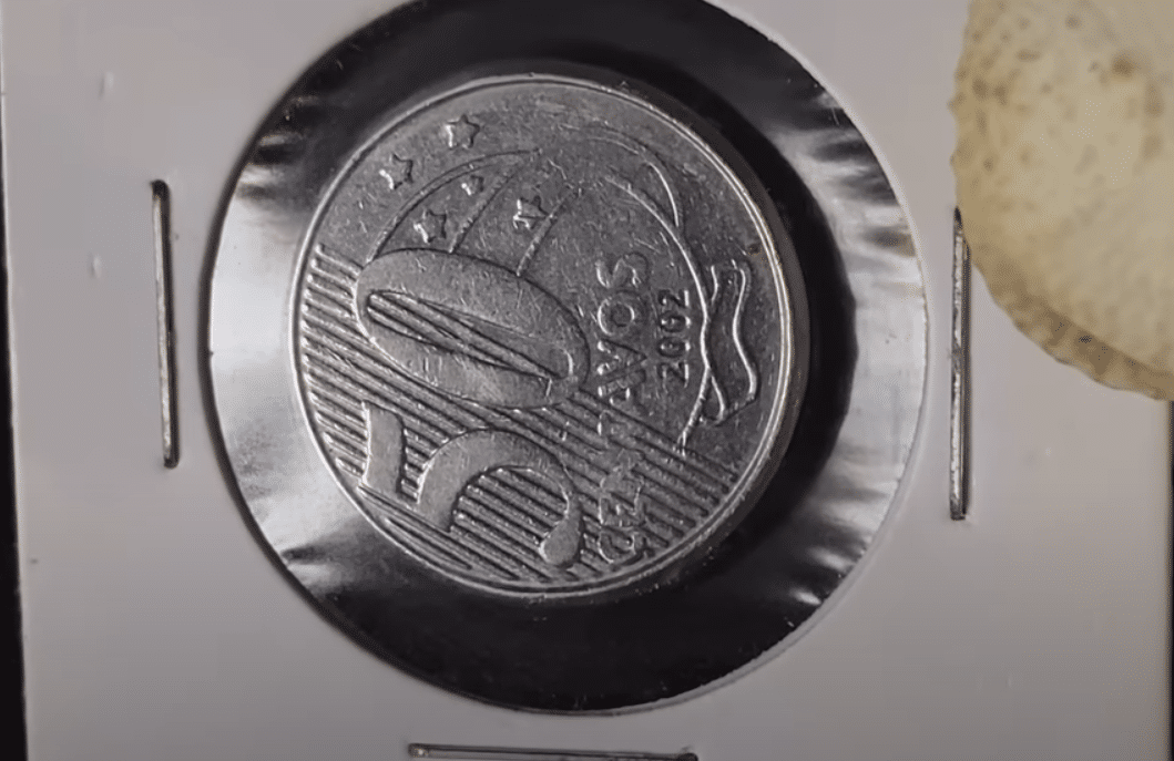 Moeda de 50 centavos do ano 2002 em protetor, representando o erro de reverso horizontal que a torna rara e muito procurada por colecionadores.