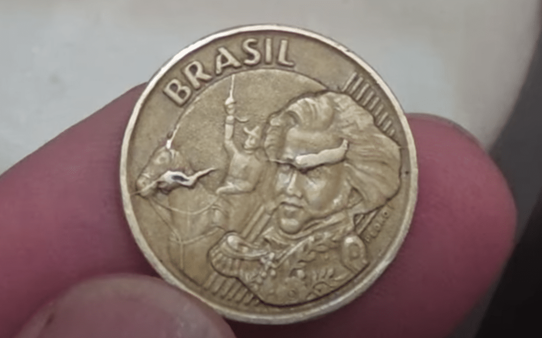 Anverso da moeda de Tiradentes (série antiga), simbolizando a busca por moedas raras e com defeitos de cunhagem, como a valiosa moeda de 10 centavos de 2001.