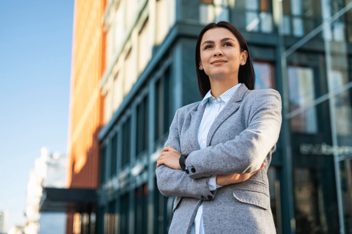 Mulher de negócios com postura confiante em frente a um prédio moderno, simbolizando o sucesso nas carreiras em alta de 2025 (tecnologia, saúde, gestão e sustentabilidade).