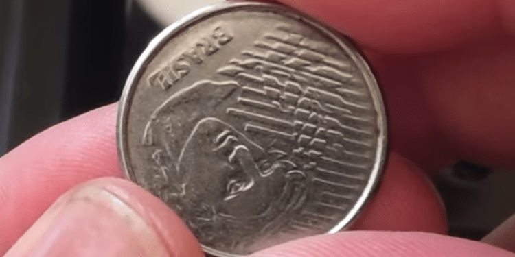 Mãos segurando a moeda de 5 centavos do Brasil, inspecionando o anverso. Representa a busca pelo raro erro de reverso invertido de 1994, que pode valer R$ 120,00.