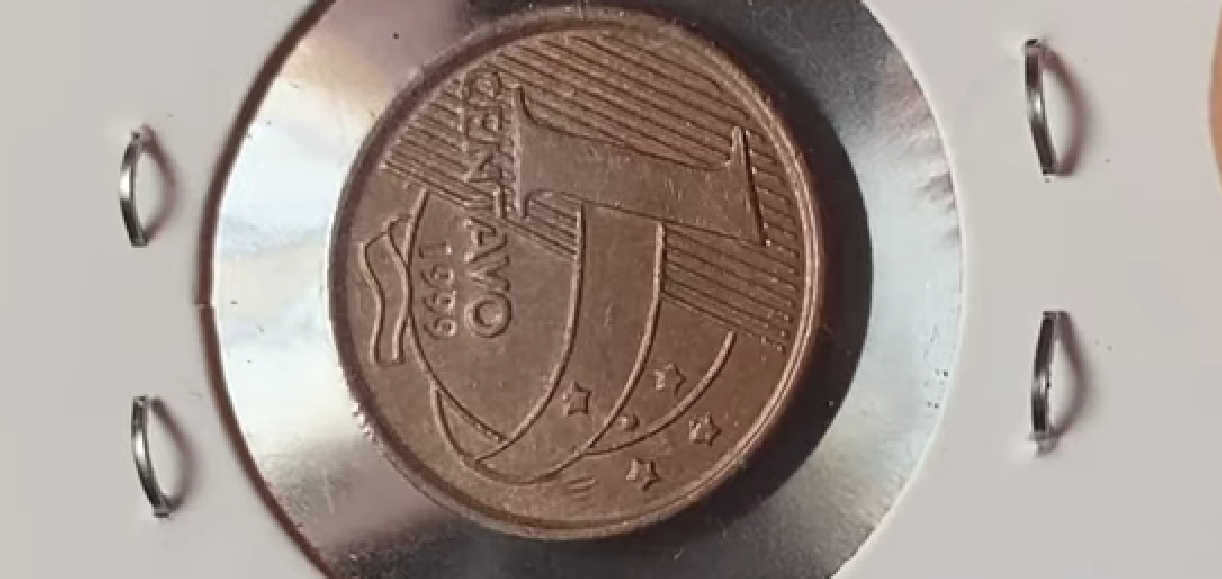 Moeda de 1 centavo sendo segurada, exibindo o detalhe do reverso horizontal, um raro e valioso erro de cunhagem que aumenta seu valor para colecionadores de numismática.