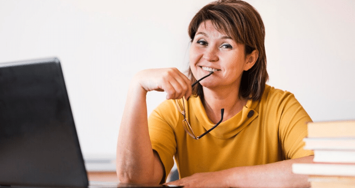 Mulher madura sorrindo e estudando em frente a um laptop, simbolizando a requalificação profissional e a busca pelo primeiro emprego após os 40 anos através de cursos gratuitos.