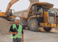Técnico em Mineração com capacete e colete refletivo em canteiro de obras, em frente a máquinas pesadas.