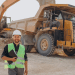 Técnico em Mineração com capacete e colete refletivo em canteiro de obras, em frente a máquinas pesadas.