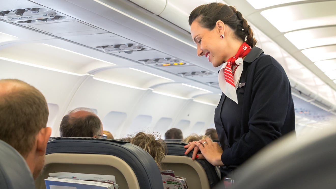 Comissária de bordo sorrindo e atendendo passageiros na cabine de um avião, ilustrando uma das profissões mais cobiçadas, que exige comunicação, serviço ao cliente e viagens.