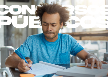 Jovem vestindo camiseta azul estudando para concursos em mesa com livros e caderno.
