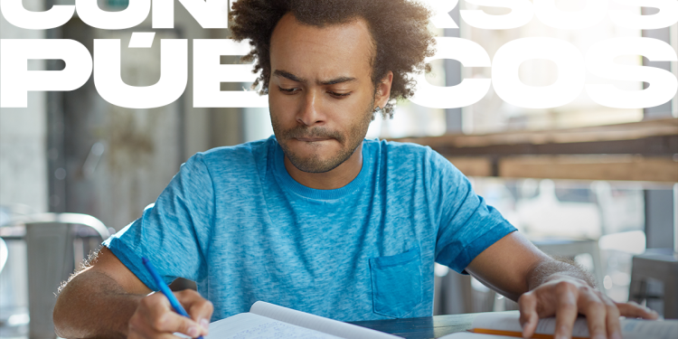 Jovem vestindo camiseta azul estudando para concursos em mesa com livros e caderno.