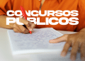 Pessoa escrevendo em caderno com caneta vermelha, estudando para concurso público.
