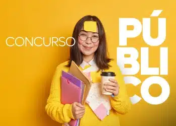 Jovem sorridente com suéter amarelo e óculos, segurando cadernos e café, preparada para concurso público