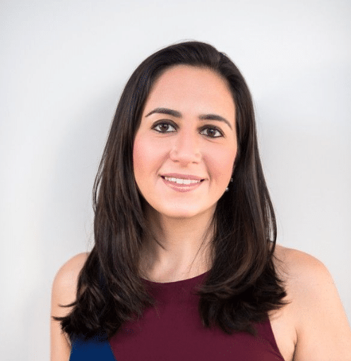 Mulher sorridente com cabelo preto liso, vestindo blusa vinho sem mangas, fundo branco