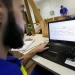 Homem com barba usando camiseta azul trabalha em notebook Samsung com software aberto em ambiente de escritório