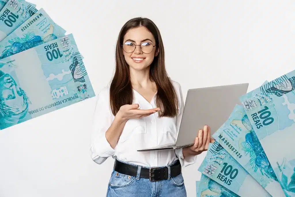 Imagem ilustrativa de uma mulher segurando um notebook e sorrindo enquanto exibe cédulas de R$100, ilustrando o sucesso financeiro sem a necessidade de diploma universitário.