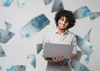 Imagem de um profissional sorrindo enquanto trabalha em seu laptop, com notas de dinheiro ao fundo, simbolizando as oportunidades no mercado de trabalho brasileiro impulsionadas por tecnologia e sustentabilidade.
