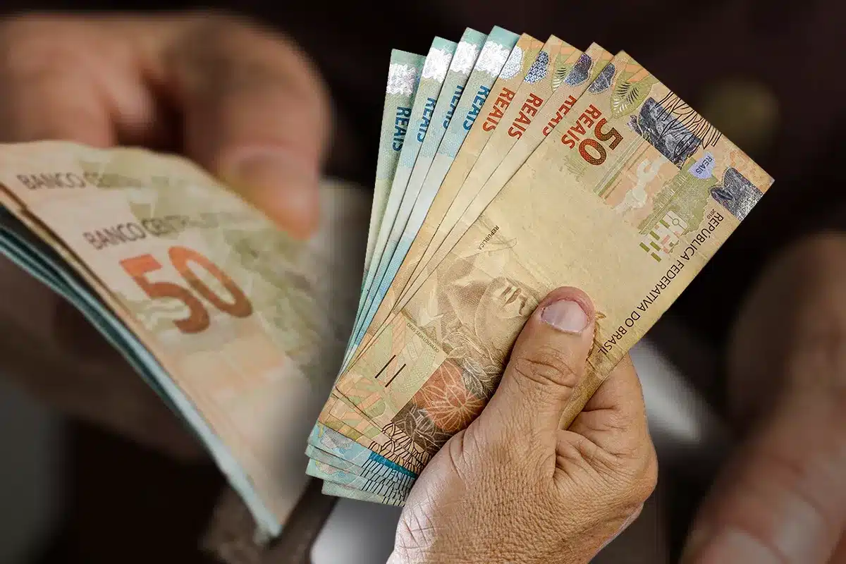 Mão segurando cédulas de real representando cronograma de pagamentos de outubro do benefício da Caixa de R$ 108