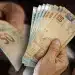 Mãos de uma pessoa contando cédulas de R$ 50 reais. Ilustra a urgência do prazo final da CAIXA para solicitar o saque de até R$ 2.800 das cotas PIS/PASEP.