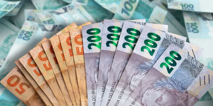 Mão segurando notas de 50, 200 e 100 reais, representando dinheiro em espécie no Brasil.