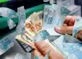 Representação visual de notas de dinheiro brasileiras, com foco nas cédulas de 100 e 50 reais, em contexto de recebimento, ilustrando os benefícios do Pé-de-Meia para o Enem 2025.