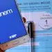 Mão segurando celular com tela do aplicativo ENEM aberto e caderno azul de prova do ENEM ao fundo